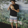 Man in tropical-themed outfit sipping coconut water against lush jungle mural.
