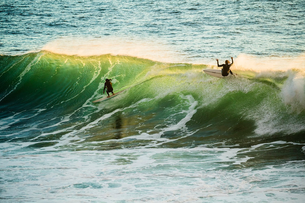 Surfers riding powerful green waves at sunset, showcasing ocean adventure.