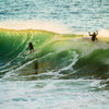 Surfers riding powerful green waves at sunset, showcasing ocean adventure.