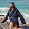 Man wearing a navy blue changing robe with a hood, walking on a sandy beach near the ocean.