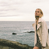 Woman in stylish trench coat by the ocean, embodying Amuse Society's chic aesthetic.