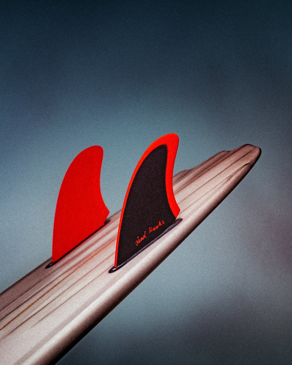 Dead Kooks surfboard with vibrant red Deflow fins against a moody backdrop.