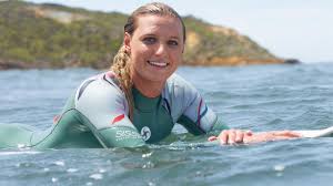 Lakey Peterson smiling while floating on a surfboard in the ocean.