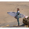 Surfer wearing the Sisstr 7 Seas wetsuit holding a surfboard on a sandy beach.