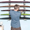 Man organizing colorful surfboards on a wall rack in a workshop. Vissla Surf