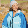 Woman wearing the White Water cobalt blue soft shell robe outdoors, showing its logo and hood.