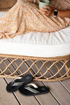FoamLife Yogi black flip flops placed on a wicker chair for a cozy look.