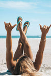 Woman relaxing on the beach wearing FoamLife Lixi flip flops in spearmint.