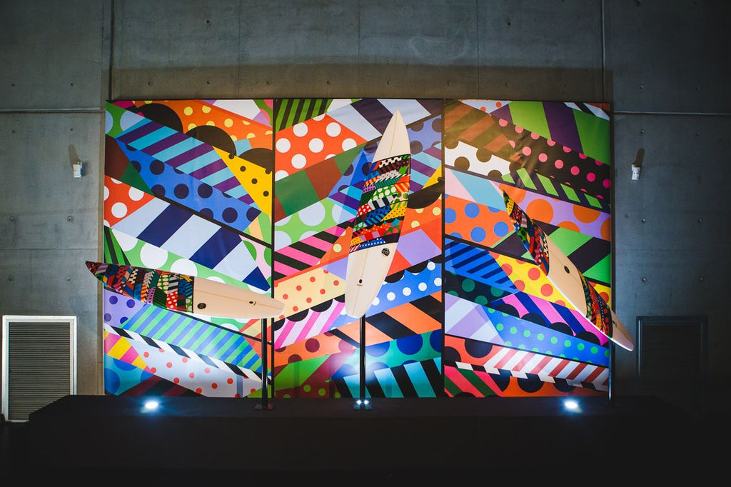 Vibrant surfboards displayed against a colorful geometric mural backdrop.