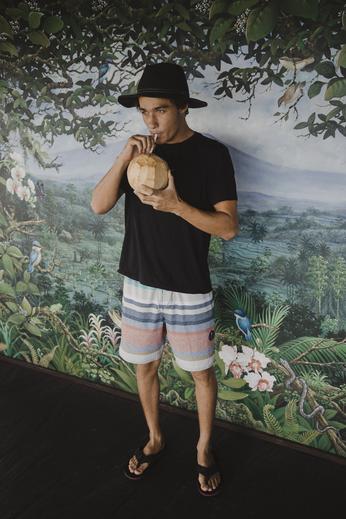 Man in tropical-themed outfit sipping coconut water against lush jungle mural.