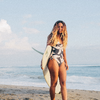 Surfer Flora at sunset holding a surfboard on the beach, Sisstrevolution.