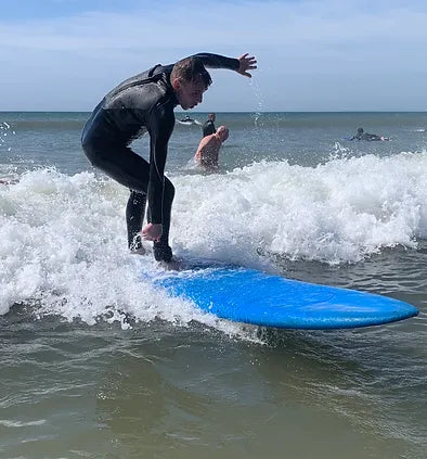 Person riding a wave on a blue surfboard during a surf therapy session.