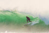Surfer riding a powerful green wave in the ocean, showcasing nature's raw energy.
