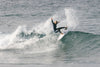 A surfer wearing a wetsuit performs a dynamic maneuver on a breaking wave.