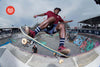 A skateboarder performs a stylish grind on a bowl edge at a vibrant skatepark.