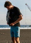 Man wearing Vissla Solid Sets 17.5" Ecolastic boardshort in tidal blue on a beach.