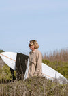 Man wearing Vissla Shaper Eco Flannel in dark sand, standing outdoors with a surfboard.