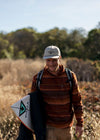 Man wearing Vissla Solar Swells Hat outdoors, holding a surfboard.