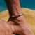 Woven Pride anklet with rainbow colors worn on an ankle by the beach.