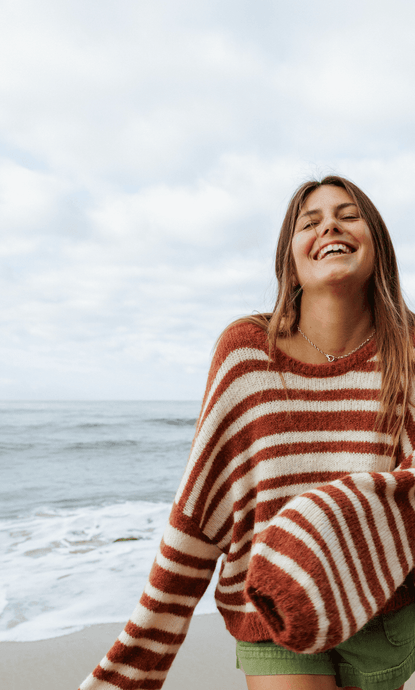 Sisstr Ocean Shores Sweater in rust with white stripes, worn by the beach.