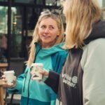 Two women enjoying coffee while wearing White Water soft shell robes, one in cobalt blue and the other in gray.